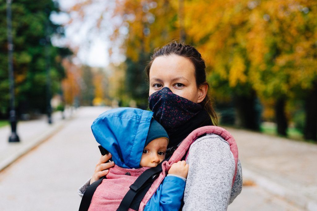 Una mujer con mascarilla llevando a un bebé en una mochila de porteo. Foto: Marcin Jozwiak, Unsplash